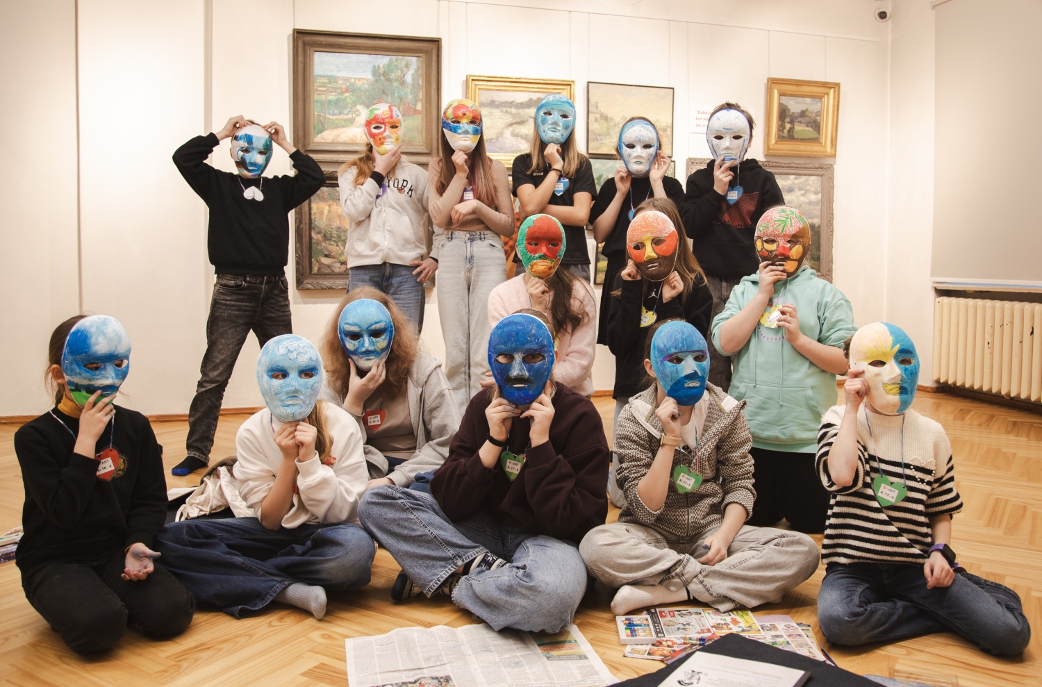 bērni izstāžu zālē pozē ar apgleznotām maskām uz sejas